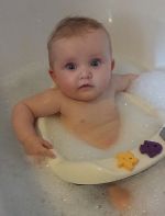 Das Bild zeigt ein weibliches Baby, das in der Badewanne sitzt. 